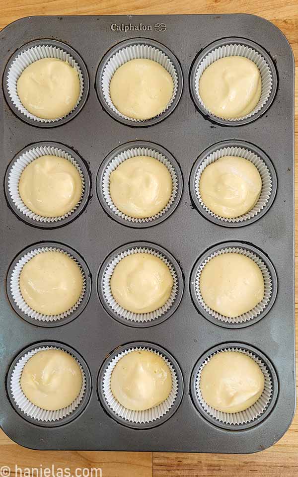 Cupcake pan lined with white liners, filled with cake batter.