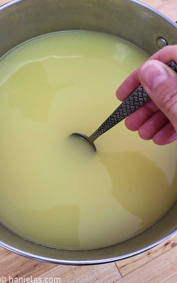 Hand holding a spoon, stirring liquid in a pot.