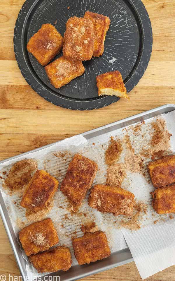 Cinnamon sugar coated fried cakes on a baking sheet lined with a paper towel.