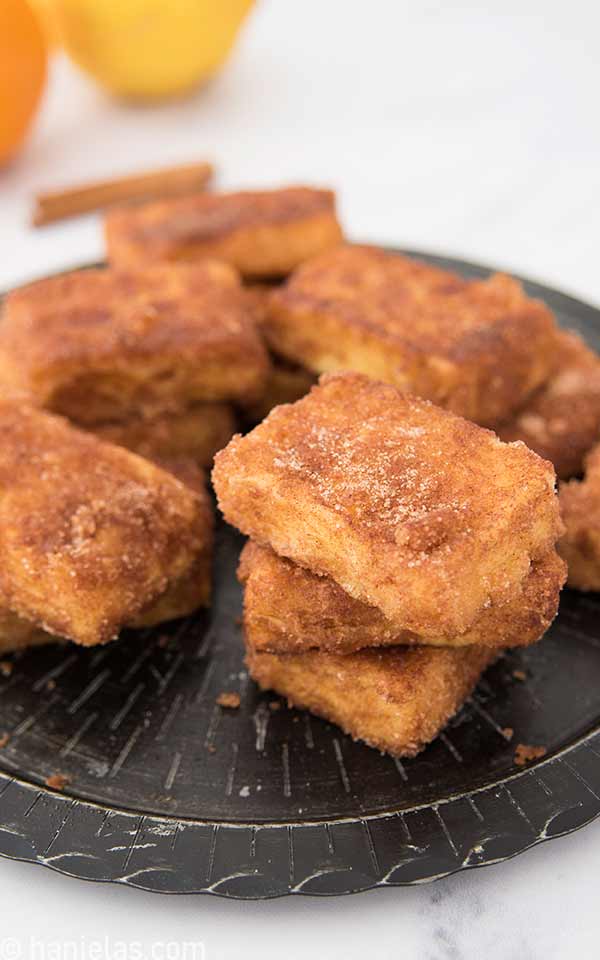 Fried cakes dipped in cinnamon sugar on a black plate.