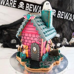 Gingerbread house decorated with pink icing, adorned with rice paper ghost, cookie bats and jack-o-lanterns.