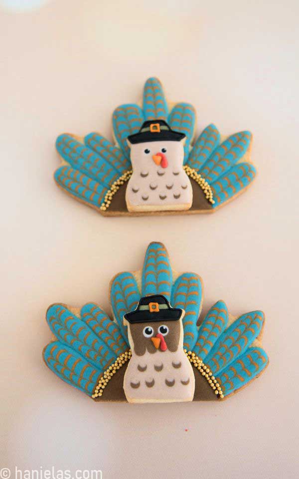 Two decorated turkey cookies in blue orange brown and black colors.
