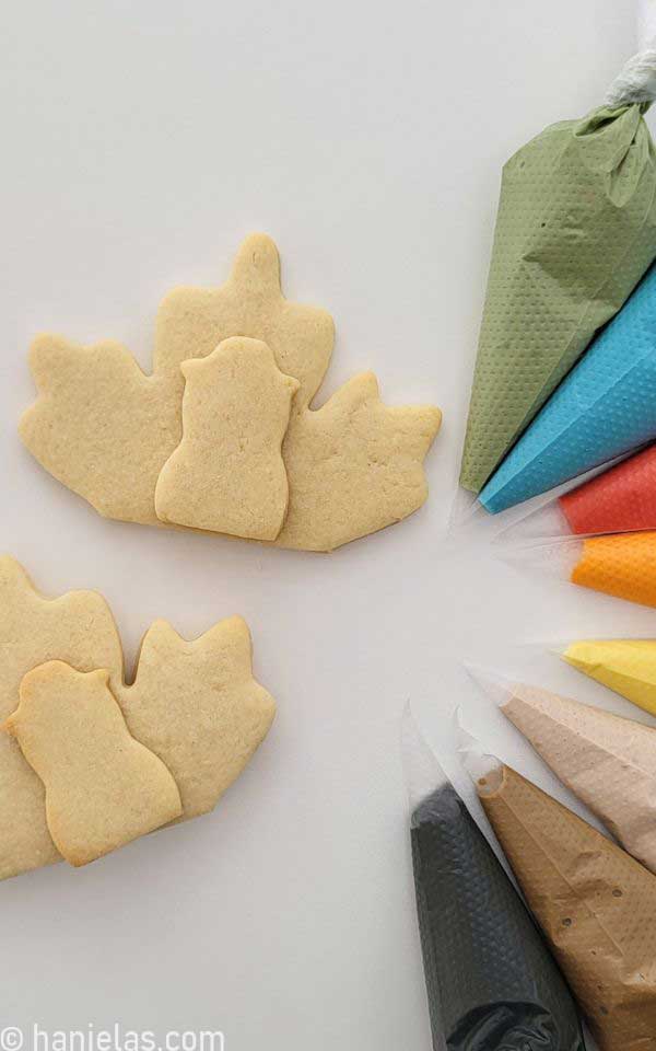 Royal icing in piping bags beside undecorated cookies