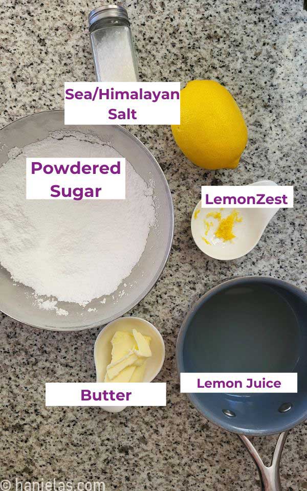 Bowls with powdered sugar, zest, butter and a small saucepan with lemon juice on a granite countertop.